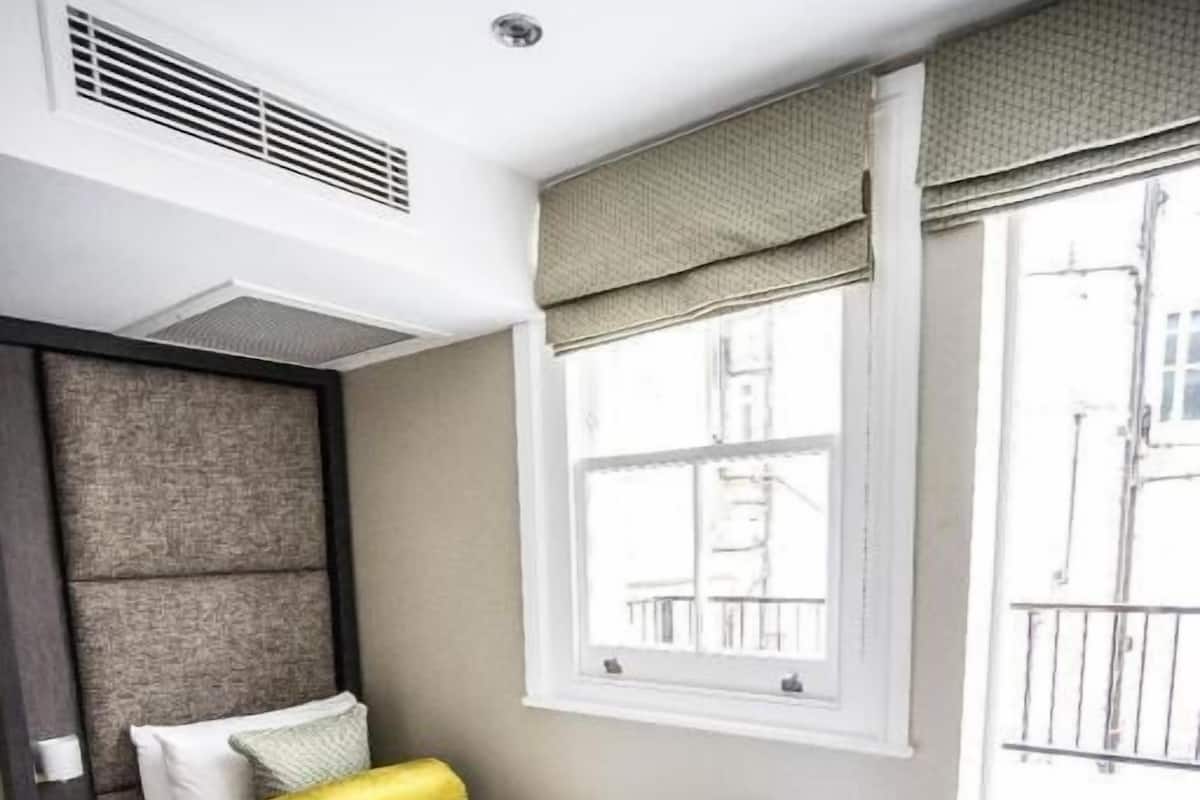 A hotel room with a bed, a window with a view, a radiator, and a door.