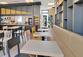 Un café moderno con varias zonas de estar, incluyendo mesas y cabinas, y una barra con una máquina de café.