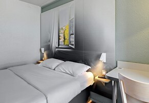 Une chambre d’hôtel moderne, équipée d’un lit, de tables de chevet, d’un miroir et offrant une vue sur une rivière et des bâtiments.