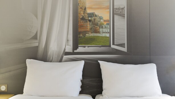 A bed with white pillows and a view of a castle through an open window. - B&B HOTEL LE MANS Centre (Le Mans)