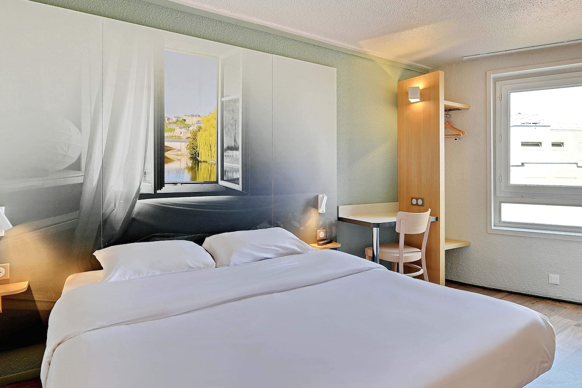 Een hotelkamer met een groot bed, een bureau en uitzicht op een gebouw door een raam.