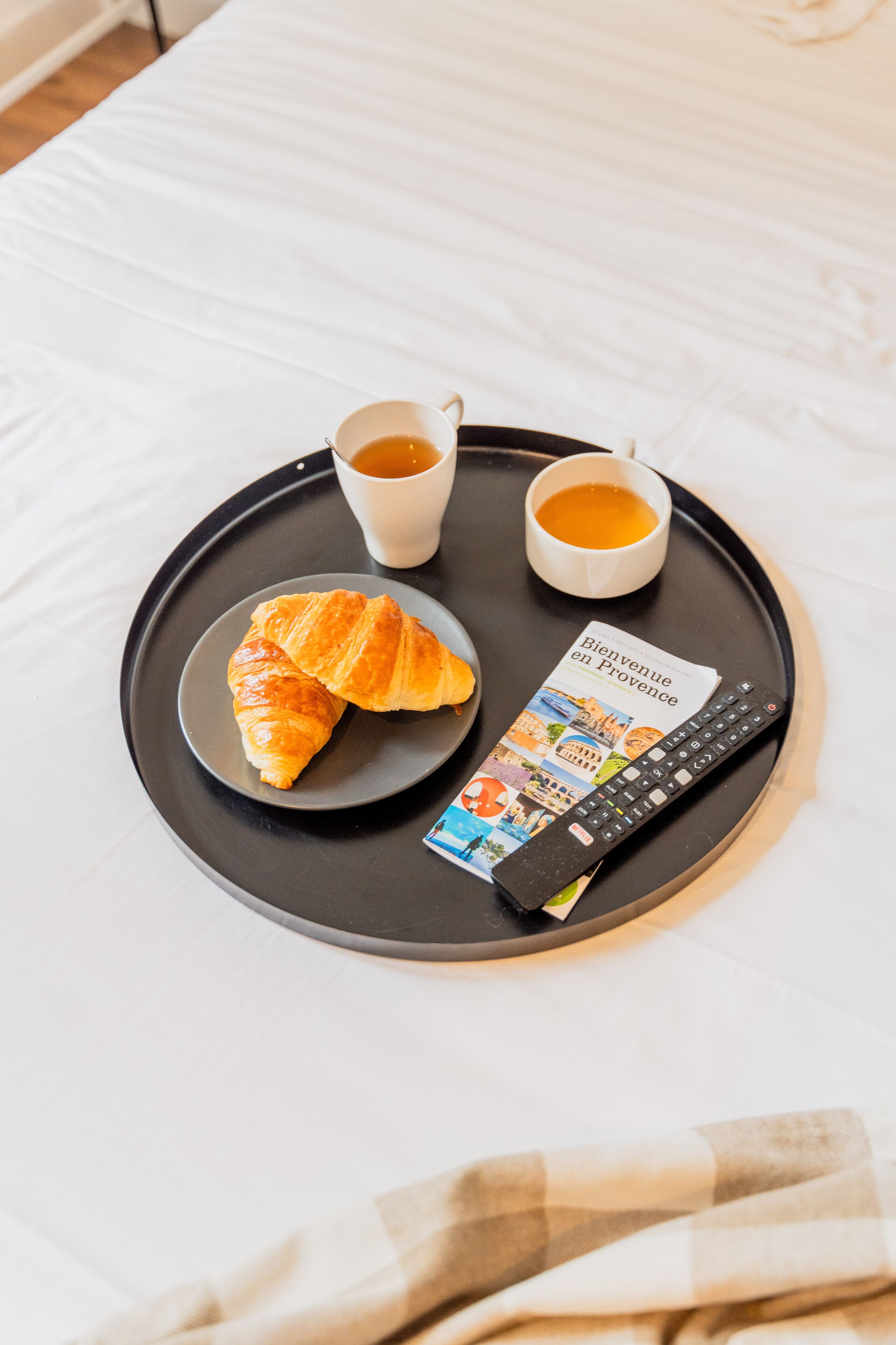 Un plateau avec des croissants, deux tasses de café et une télécommande sur un lit.