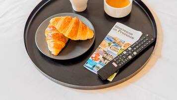 Un plateau avec des croissants, deux tasses de café et une télécommande sur un lit.
