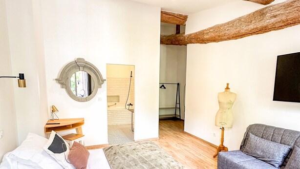 A bedroom with a bed, a sofa, a mirror, and a wooden ceiling beam. - Hôtel d'Angleterre (Salon-de-Provence)