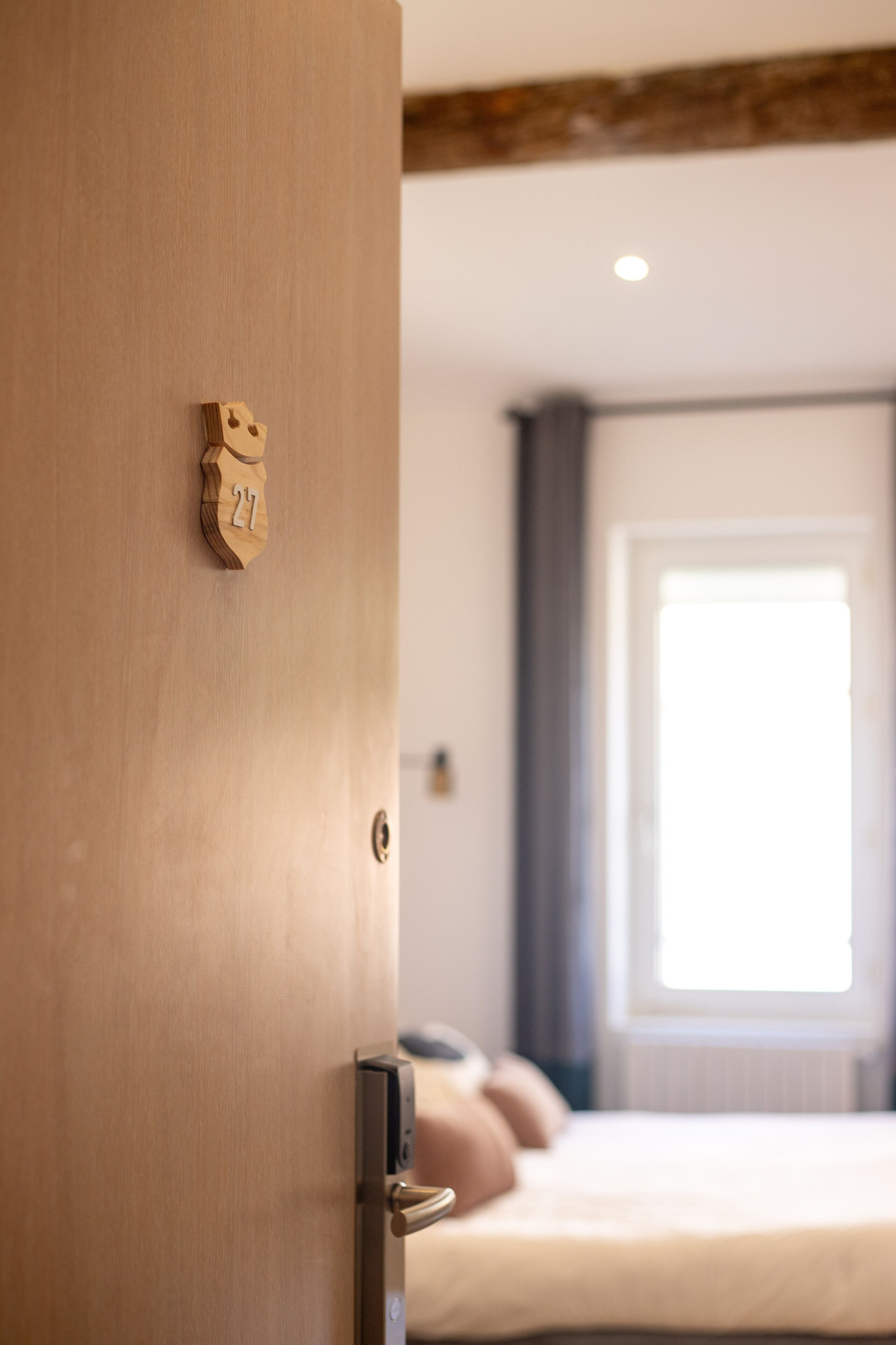 Una puerta de madera con una placa de número, una cama con almohadas y una ventana con cortinas.