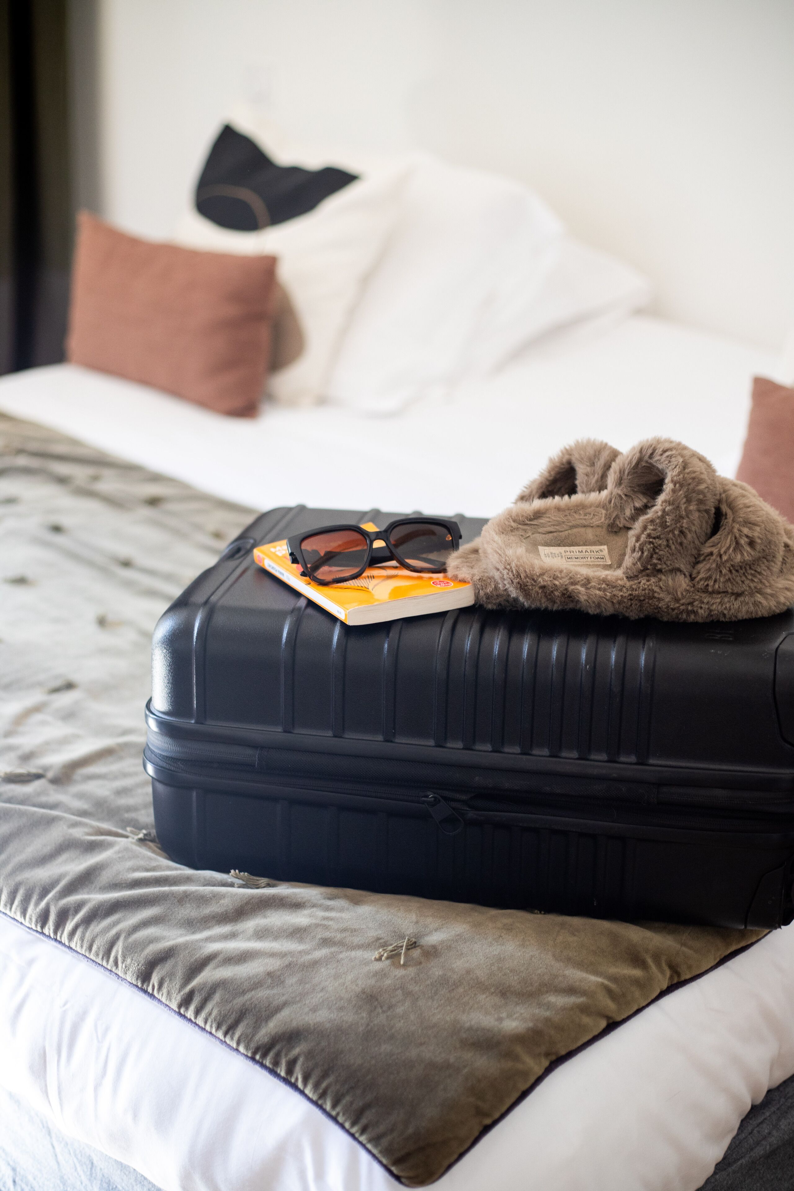 Ein Bett mit einem schwarzen Koffer, einer Brille und einem braunen Plüschtier darauf.