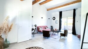 A spacious living area with a high ceiling, exposed wooden beams, a large window with curtains, and a modern sofa. - Hôtel d'Angleterre (Salon-de-Provence)
