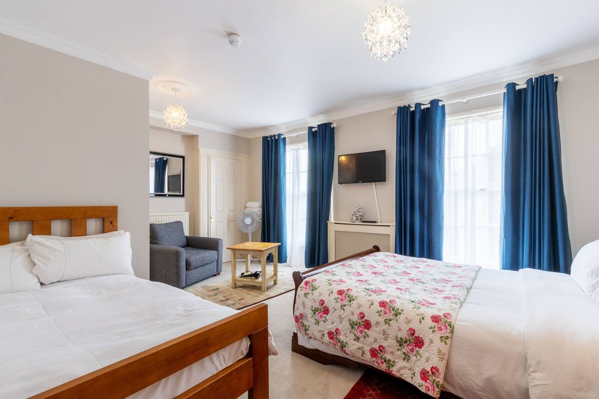 A hotel room with two beds, a TV, a fan, and a window with curtains.
