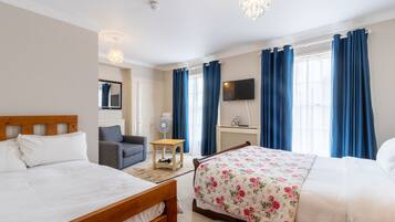 Hotellihuone, jossa on kaksi sänkyä, televisio, tuuletin ja ikkuna, jossa on verhot.