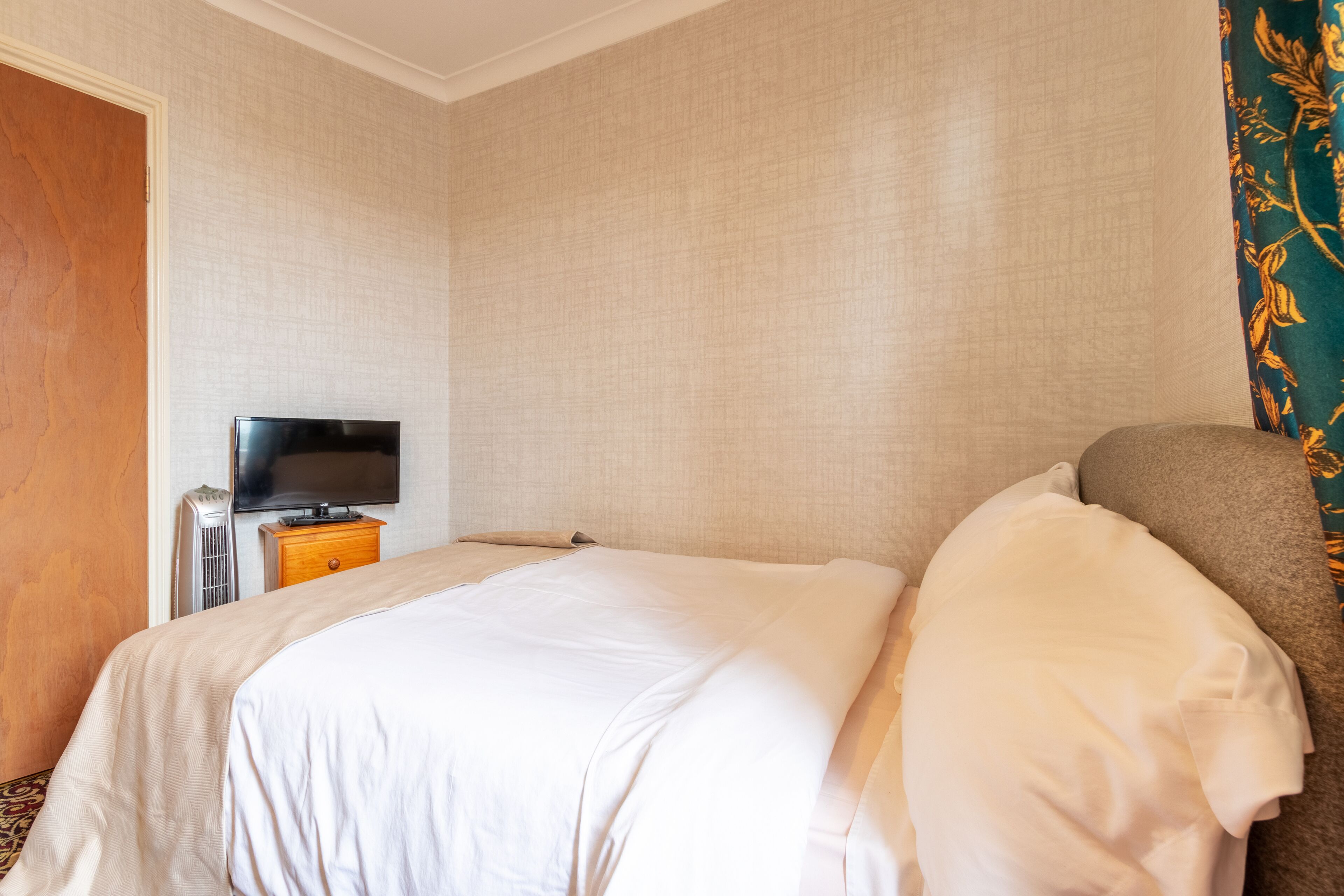 A hotel room with a bed, a television on a wooden side table, and a door.
