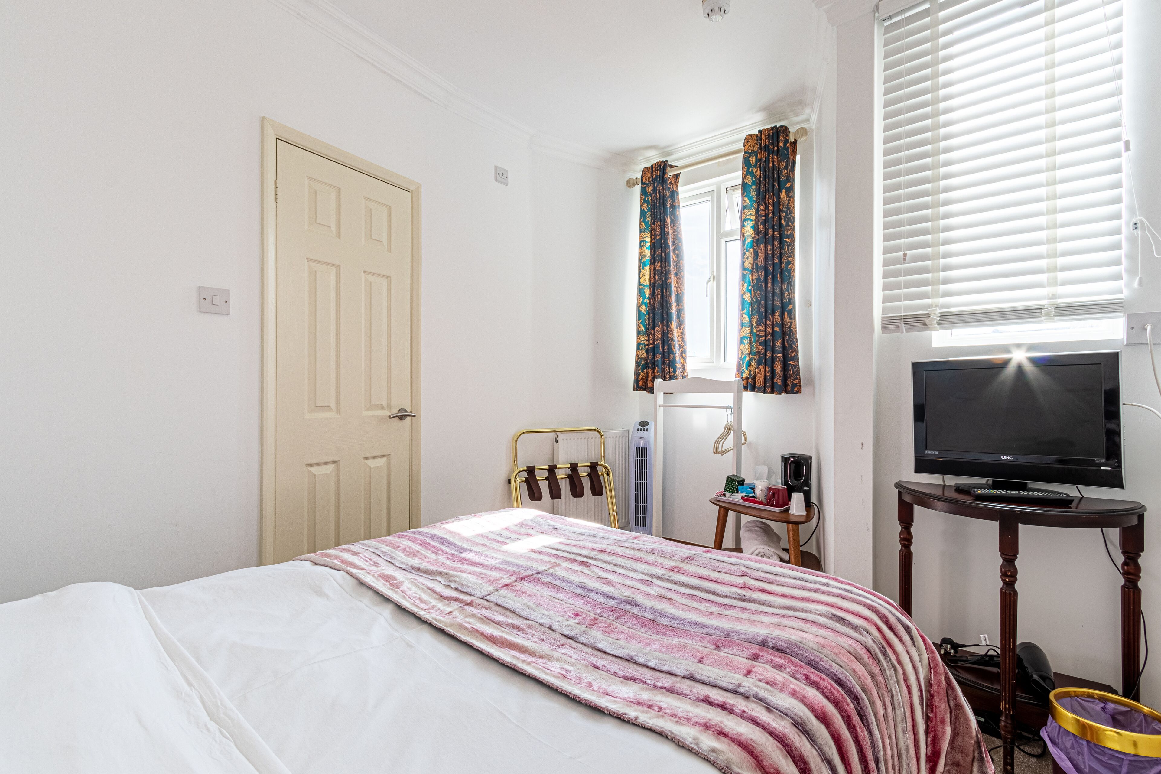 A bedroom with a bed, a television, a radiator, and a window with curtains.