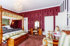 A traditional bedroom with a four-poster bed, a wooden dresser, a vanity, and a chair.