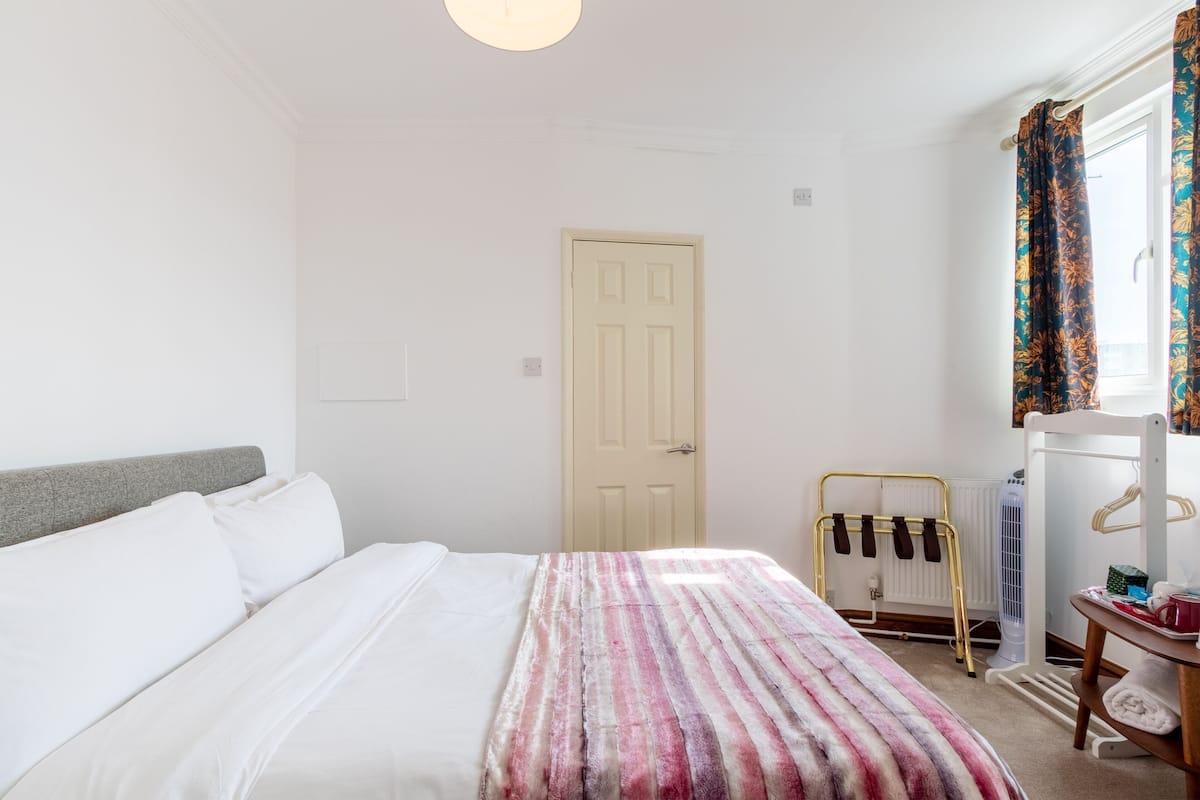A bedroom with a bed, a radiator, a window with curtains, and a door.