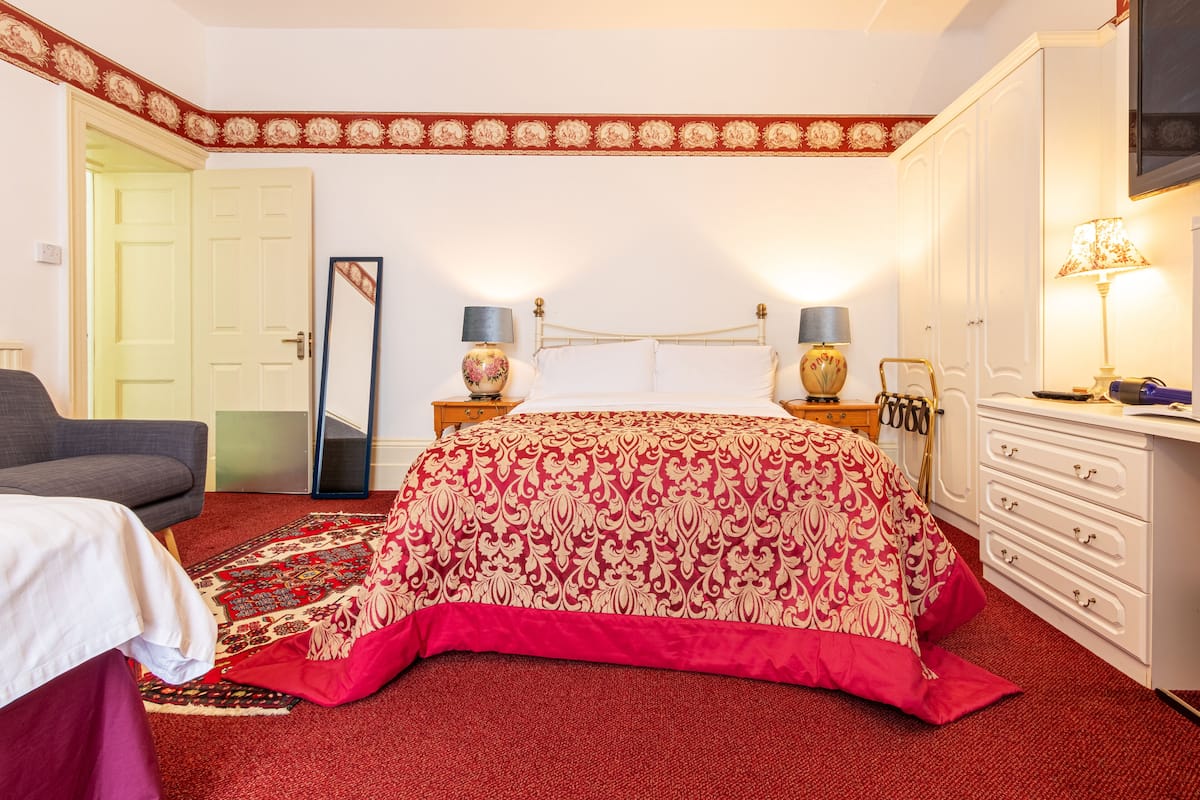 A bedroom with a large bed, a dresser, a nightstand, and a TV.