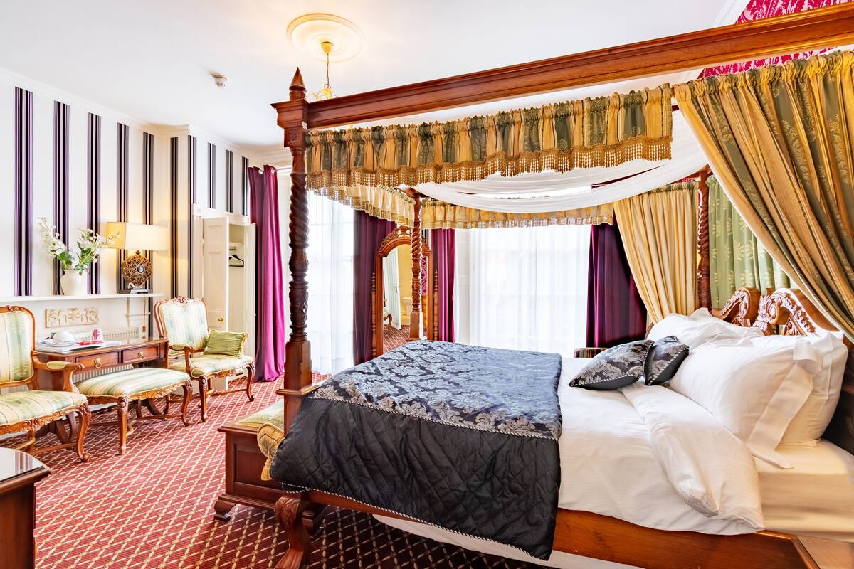 A four-poster bed with a canopy, a wooden desk with a chair, and a patterned carpet.