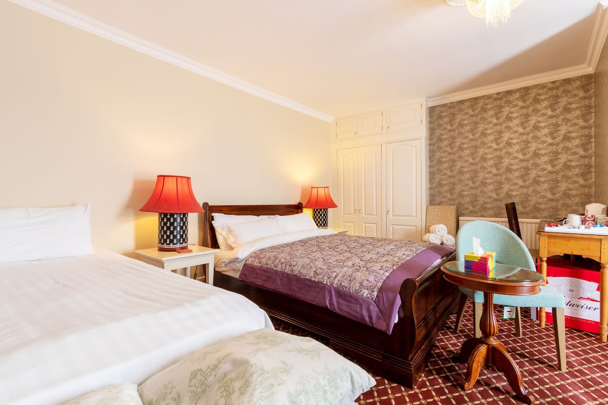 A hotel room with two beds, a desk, a chair, and a small table.