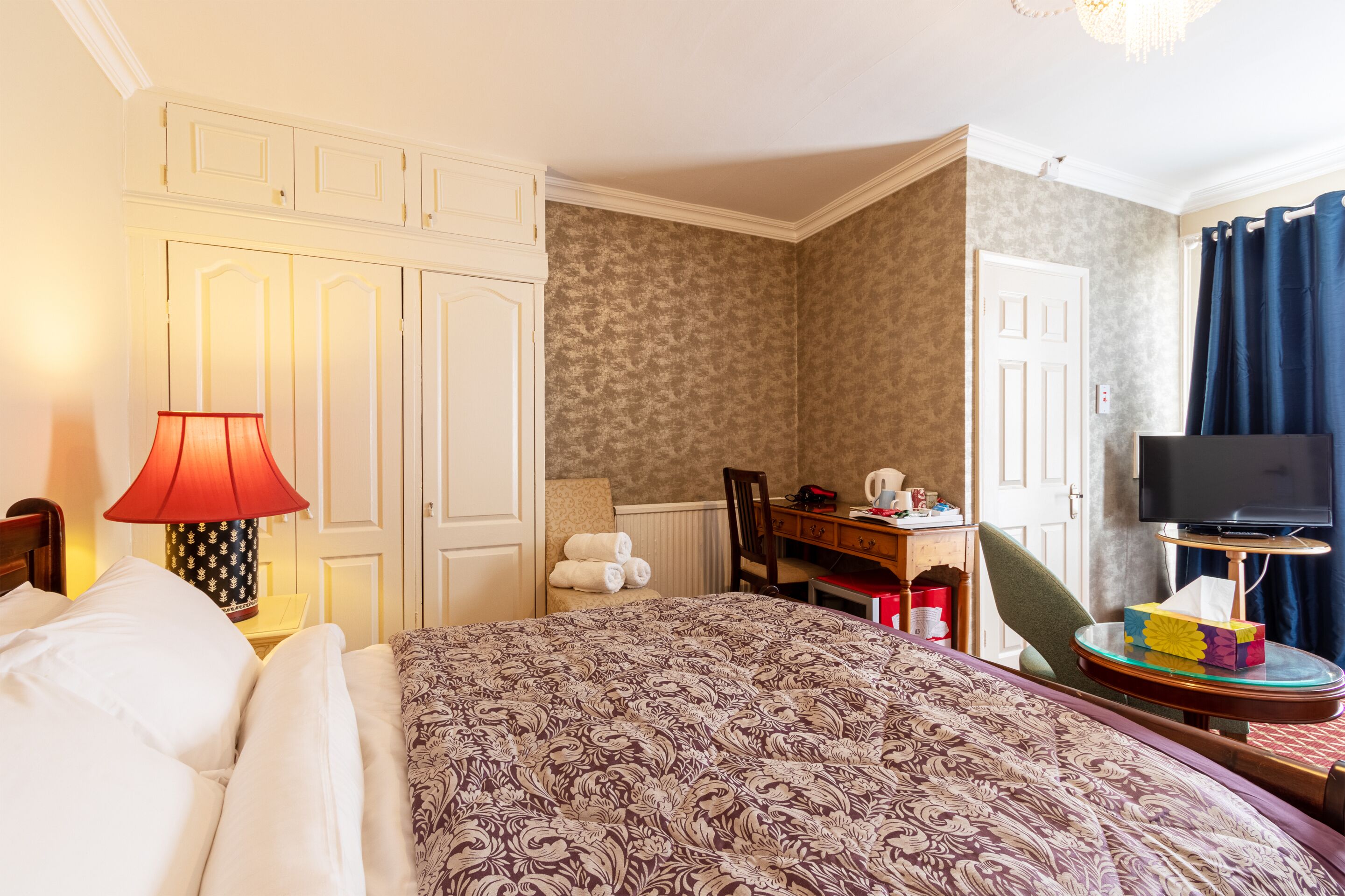 Habitación de hotel con una cama grande, un escritorio con silla, televisión y un baño visible a través de una puerta abierta.