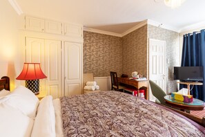 A hotel room with a large bed, a desk with a chair, a television, and a bathroom visible through an open door.
