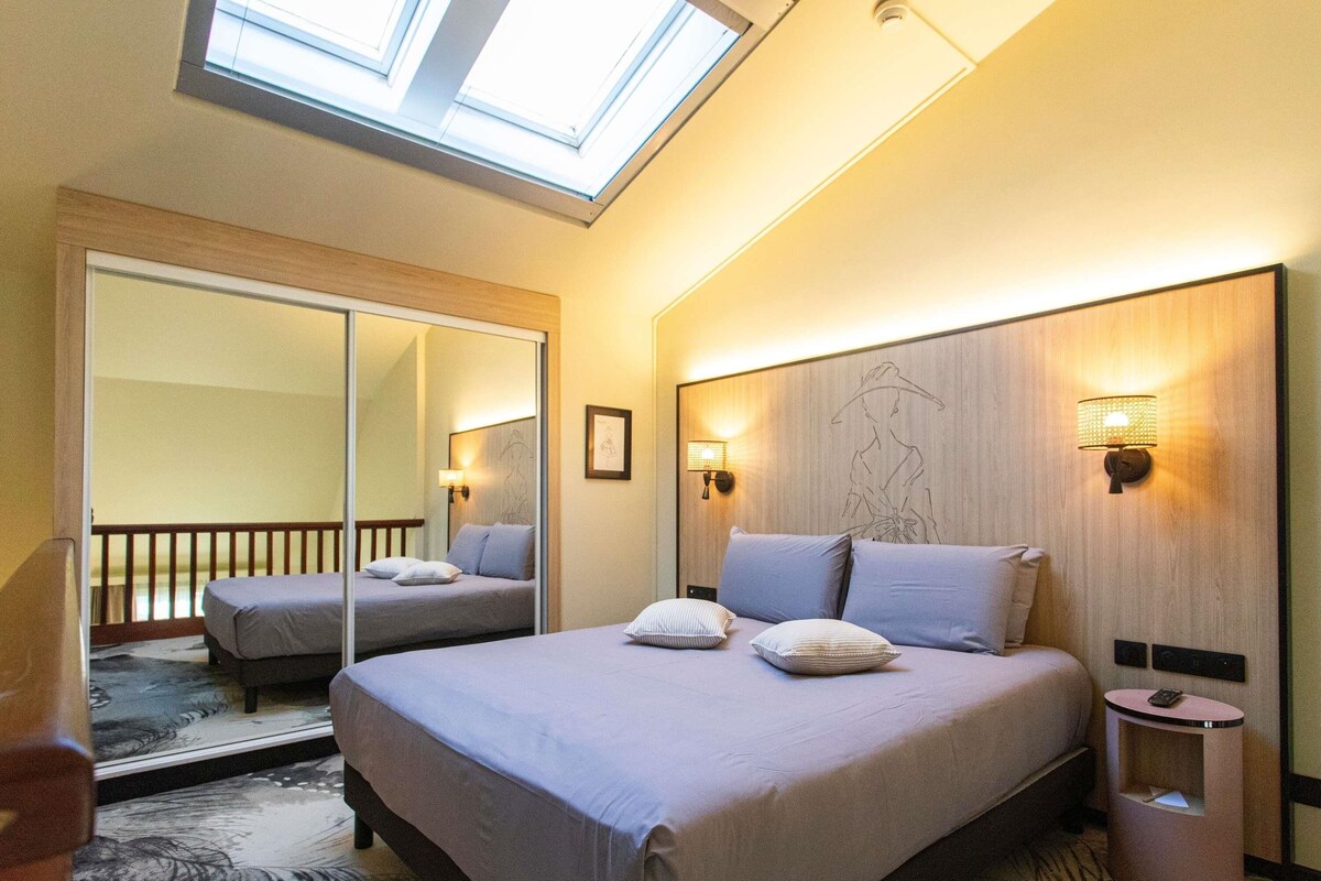 A hotel room with a large bed, a mirror, a small bedside table, and a skylight.