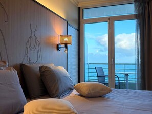 A hotel room with a large bed, a wall-mounted lamp, and a balcony with a view of the sea. - Mercure Granville Le Grand Large (Granville)