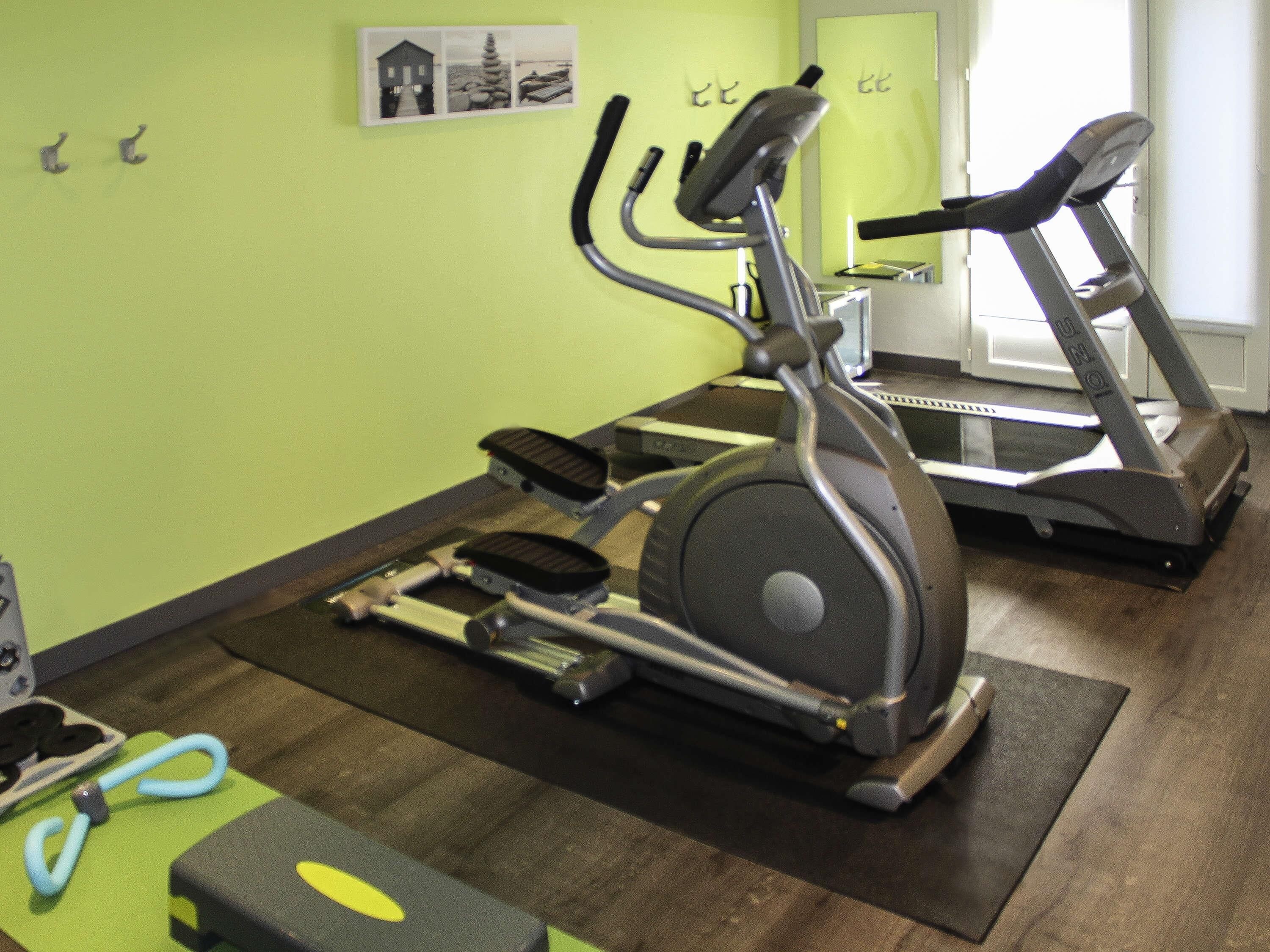 Un gimnasio con bicicletas estáticas y cintas de correr, una pared verde y un espejo.