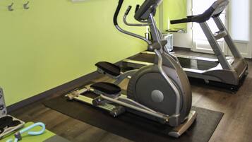 Un gimnasio con bicicletas estáticas y cintas de correr, una pared verde y un espejo.
