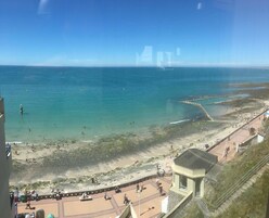 Vista costeira com praia, calçadão e um pequeno pavilhão.