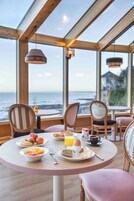 Mesa de café da manhã com diversos pratos e vista para o oceano.