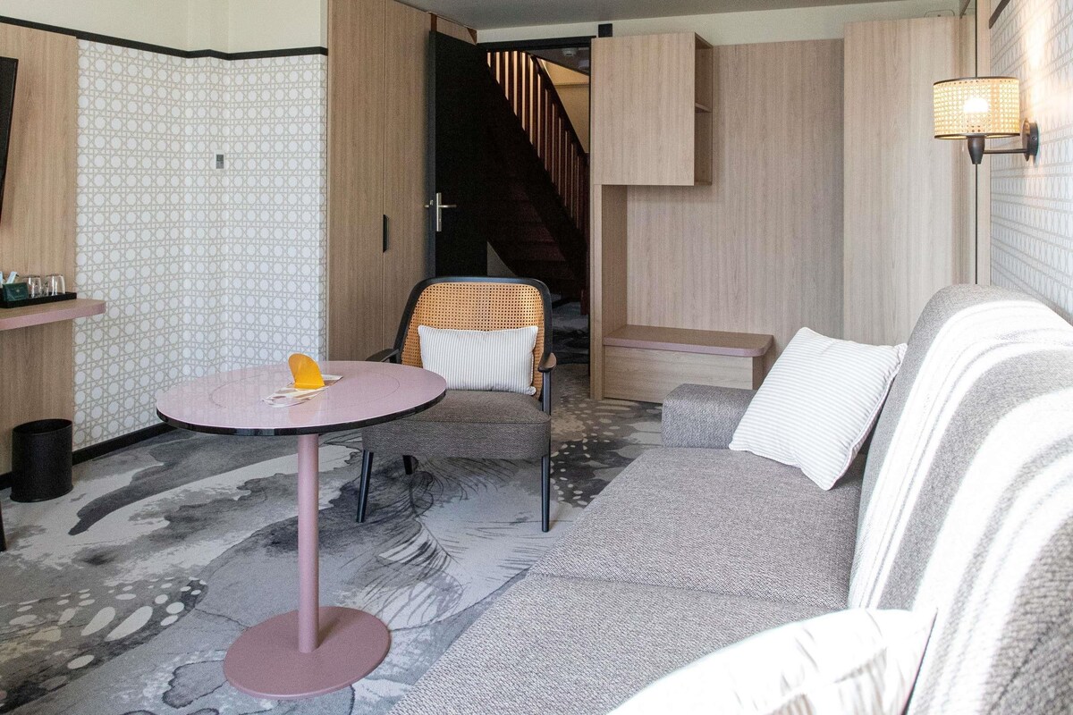 A modern room with a sofa, a round table, and a chair. There is a staircase in the background.