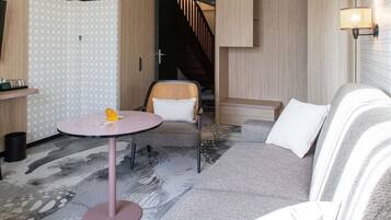 Ein modernes Zimmer mit einer Couch, einem runden Tisch und einem Sessel. Im Hintergrund ist eine Treppe zu sehen.