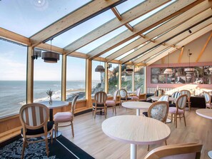 Un restaurant avec vue sur l’océan, un intérieur en bois et des tables rondes.