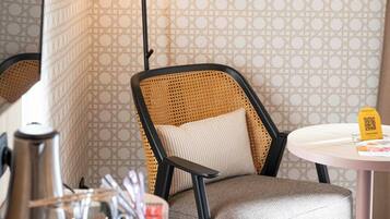 Une pièce avec un papier peint à motifs, une chaise en osier, une table dotée d’un code QR et un lampadaire.