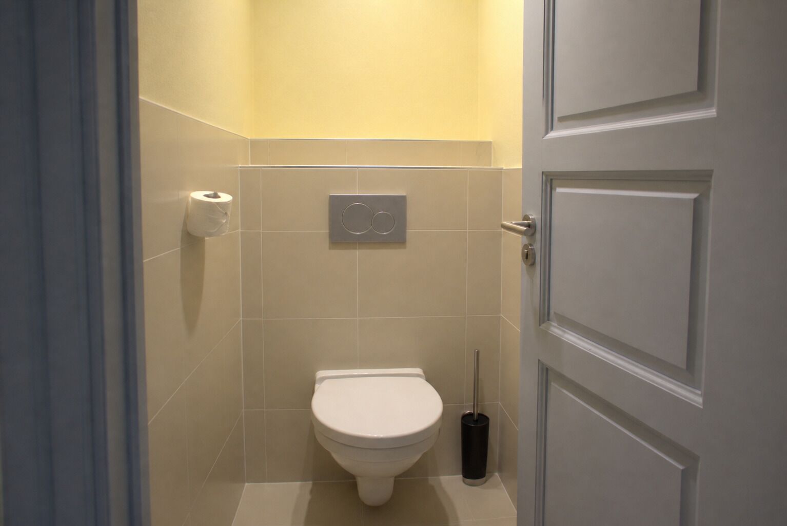 Une petite salle de bain fermée, équipée de toilettes, d’un porte-rouleau de papier toilette et d’une poubelle.
