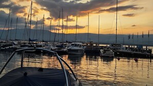 Uma marina com vários barcos atracados, céu claro e montanhas ao longe.