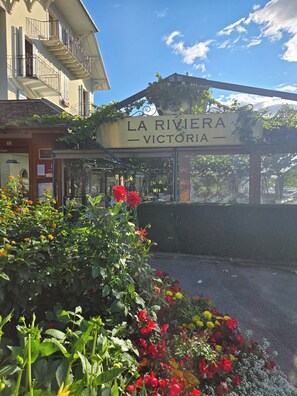 Señal de 'LA RIVIERA VICTORIA' con un edificio al fondo y un jardín en primer plano.