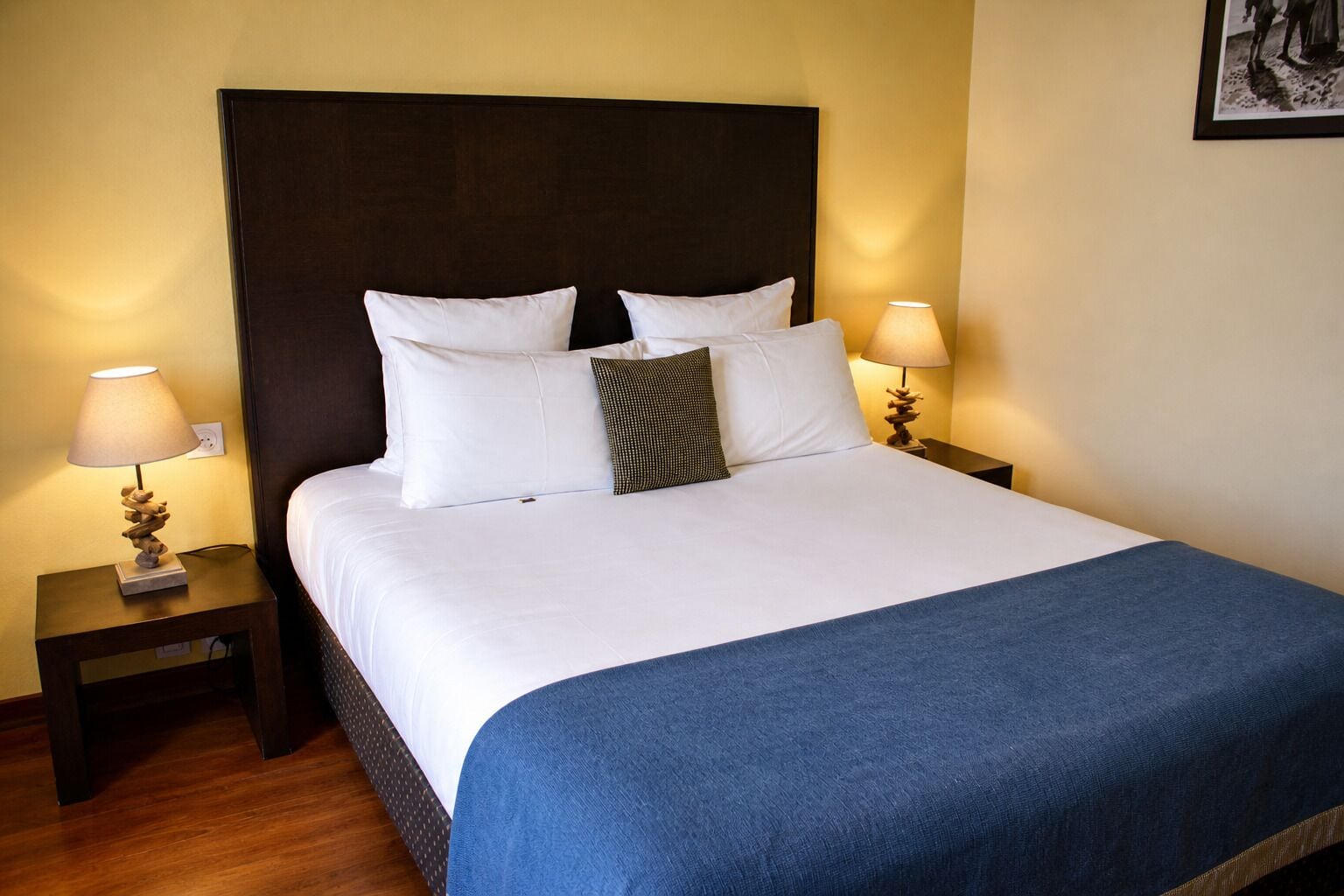 A neatly made bed with white linens, a blue throw blanket, and two bedside lamps with decorative bases.