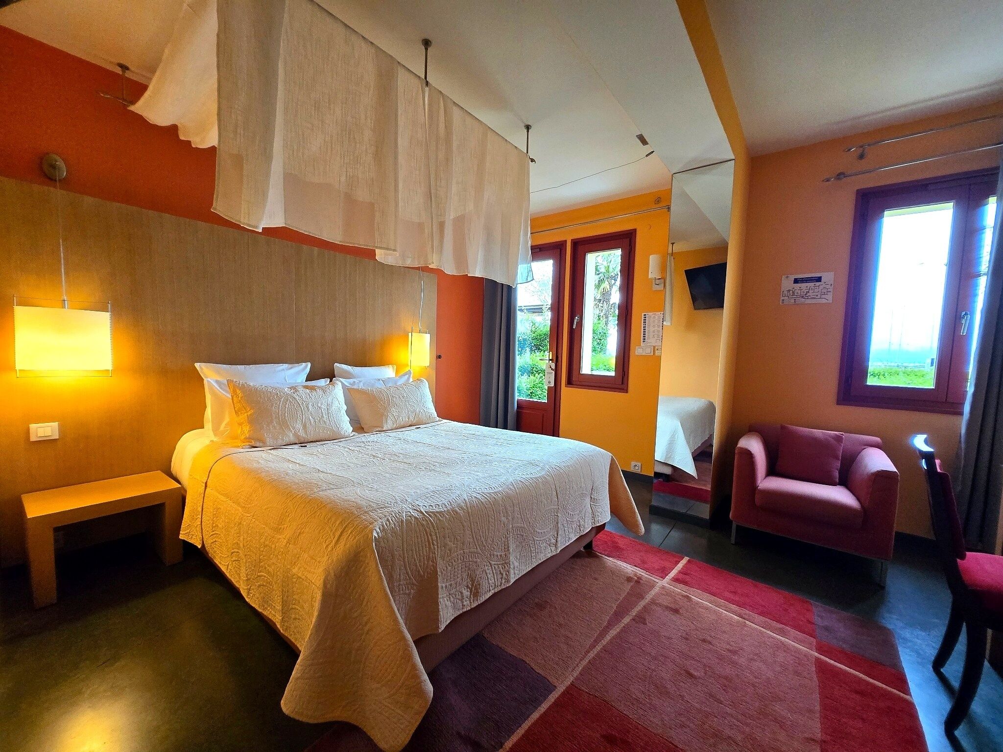A hotel room with a large bed, bedside lamps, a desk, a chair, and a window with a view.