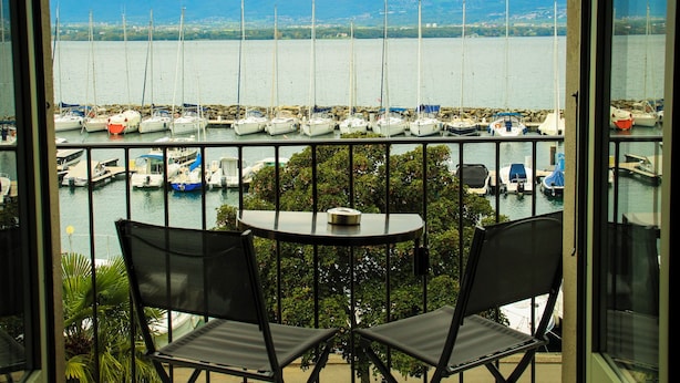 Uma varanda com duas cadeiras, uma mesa e vista para uma marina com barcos e montanhas ao longe.