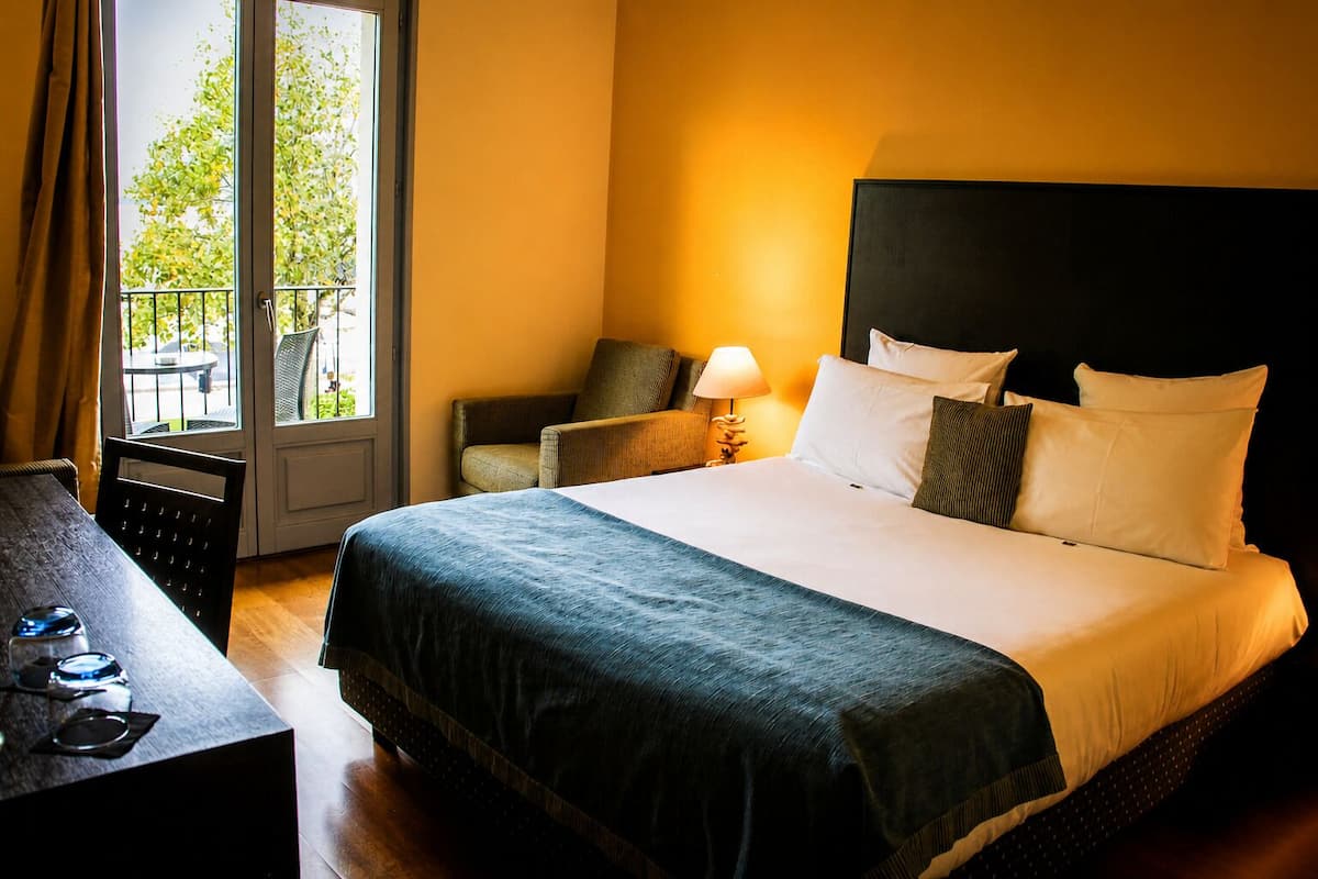 Ein Hotelzimmer mit Bett, Schreibtisch, Stuhl und einem Fenster mit Blick auf Bäume.