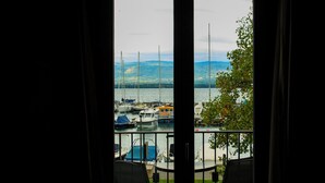 Uma varanda com duas cadeiras, vista para uma marina com barcos e uma cadeia montanhosa ao longe.