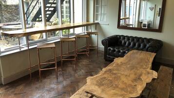 Een kamer met een grote houten tafel, een zwarte leren bank en een raam met uitzicht op een trap en groen buiten.
