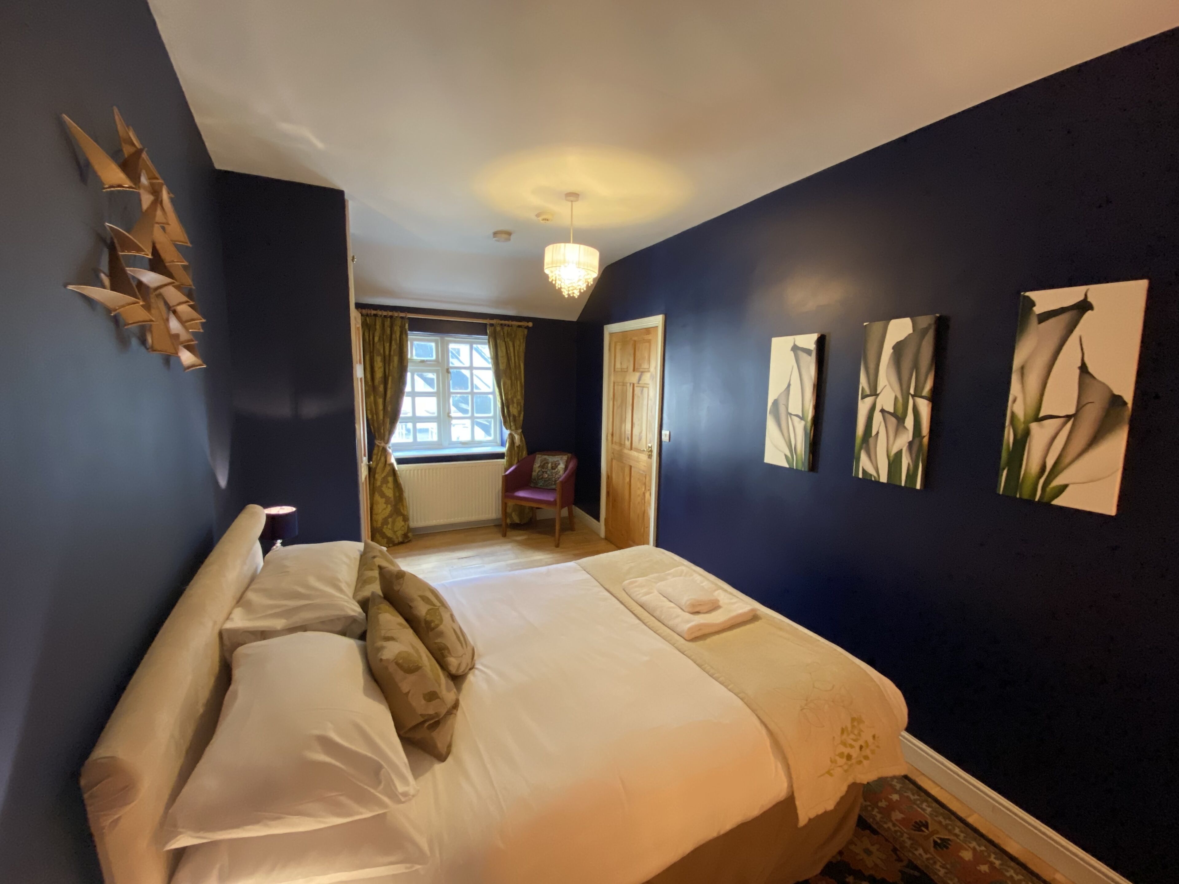 Un dormitorio con cama, una silla, ventana con cortinas y decoración en la pared.