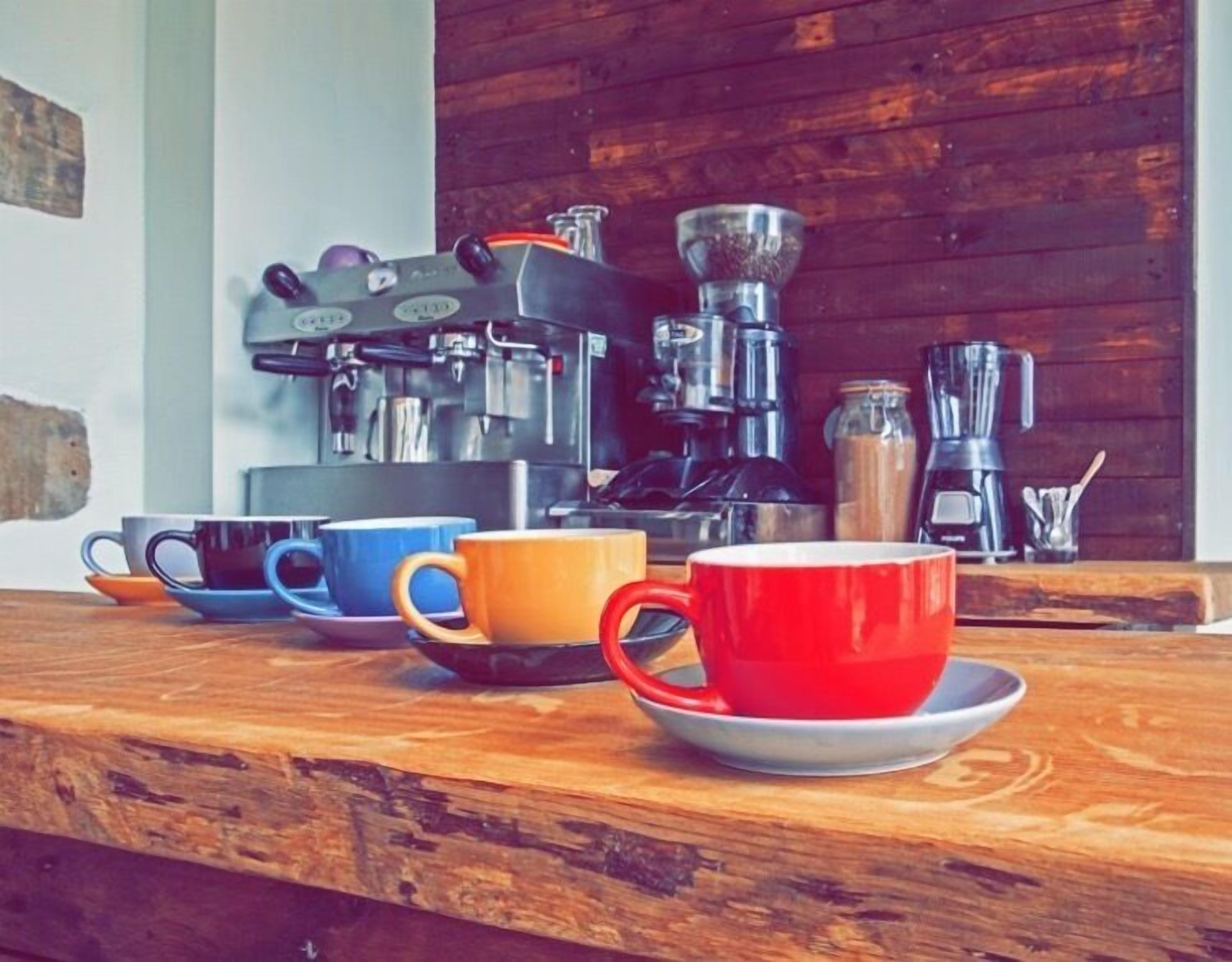 A coffee station with various coffee-making equipment and colorful cups on a wooden counter.