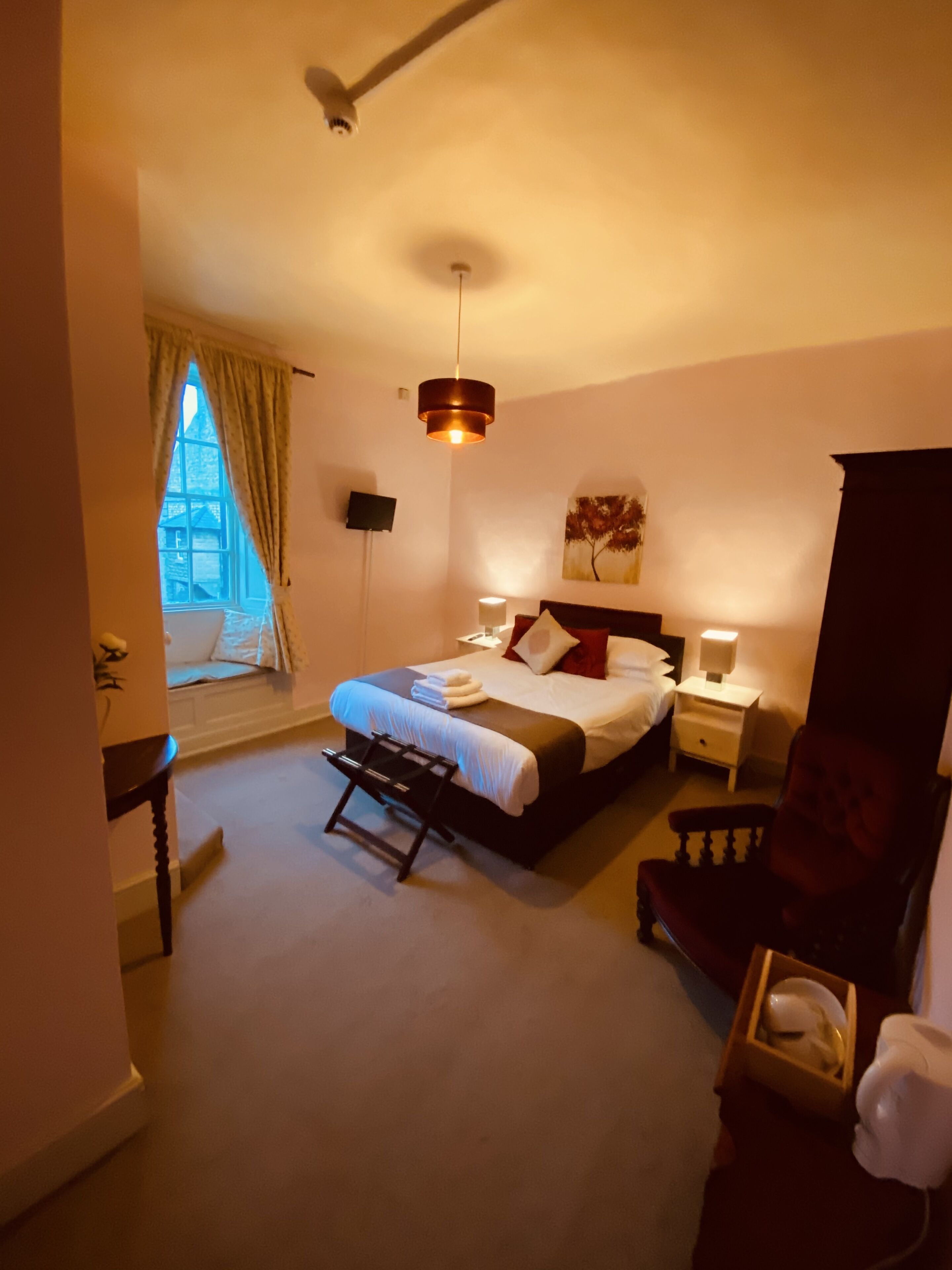 A bedroom with a bed, bedside tables, a chair, a desk, a window with curtains, and a ceiling fan.