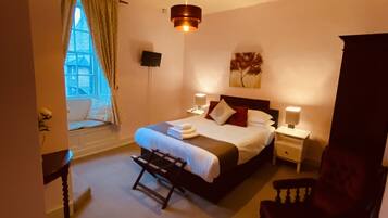 A bedroom with a bed, bedside tables, a chair, a desk, a window with curtains, and a ceiling fan.