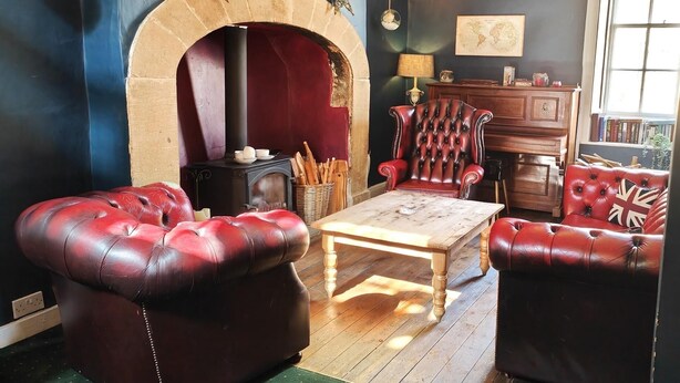A cozy living room with a fireplace, leather sofas, a wooden coffee table, and a bookshelf. - Kings Head Hotel (York)