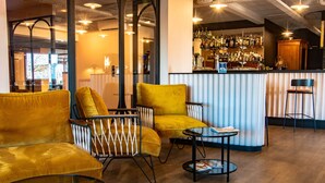 Un espace bar comprenant un comptoir, des tabourets de bar et un coin salon avec des chaises jaunes et une table.