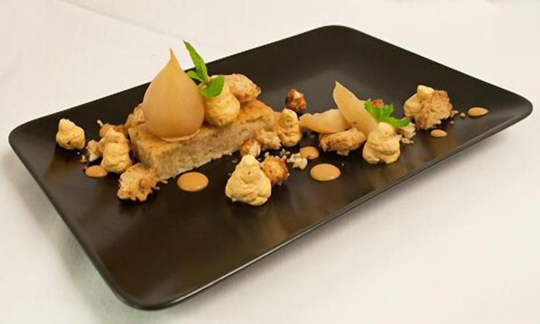 A rectangular black plate with a dessert consisting of crumbled cake, nuts, and a decorative element on top.