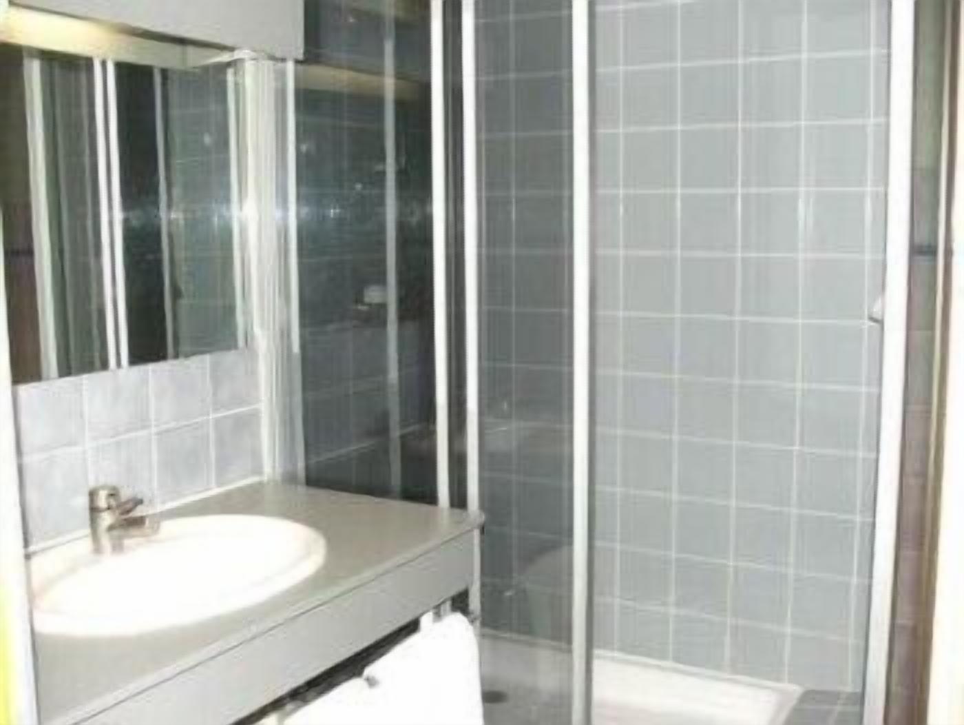 A bathroom with a glass shower enclosure, a sink with a mirror, and tiled walls.