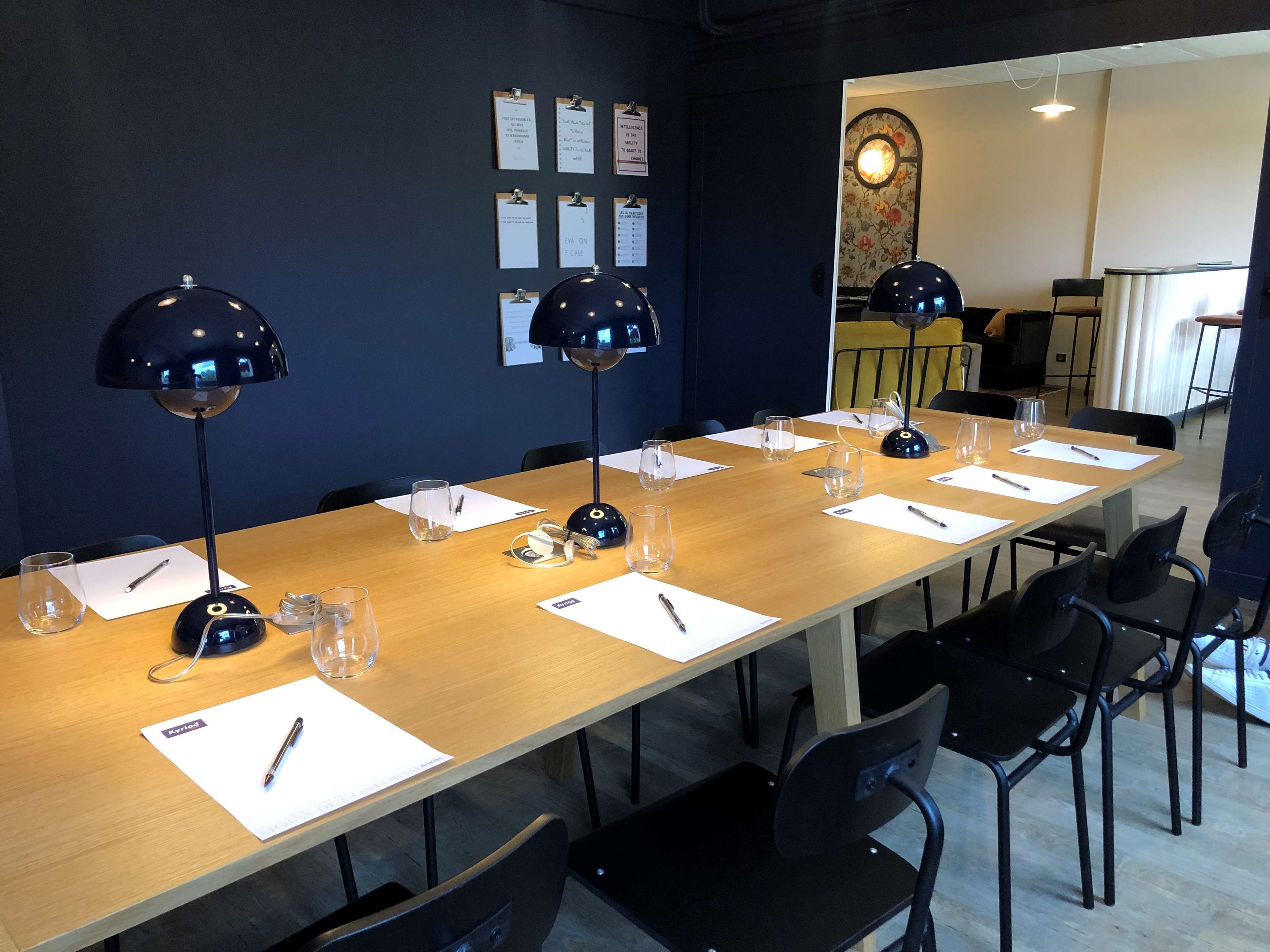 Un salón de conferencias con una larga mesa, sillas negras y tres lámparas de escritorio negras.